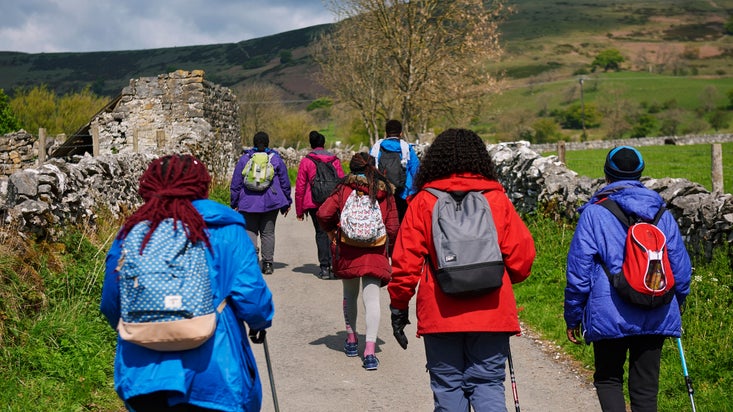 A group of people walking on a path with views of the peak district moors in the background and drystone walls alongside the path